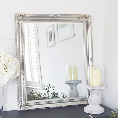 A silver wall mirror with decorative carved Fleur De Lis detailed chunky silver frame for a chic style to any bedroom, living room, hall or bathroom. The mirror can be wall hung or simply rest on a table top for dressing or console table.