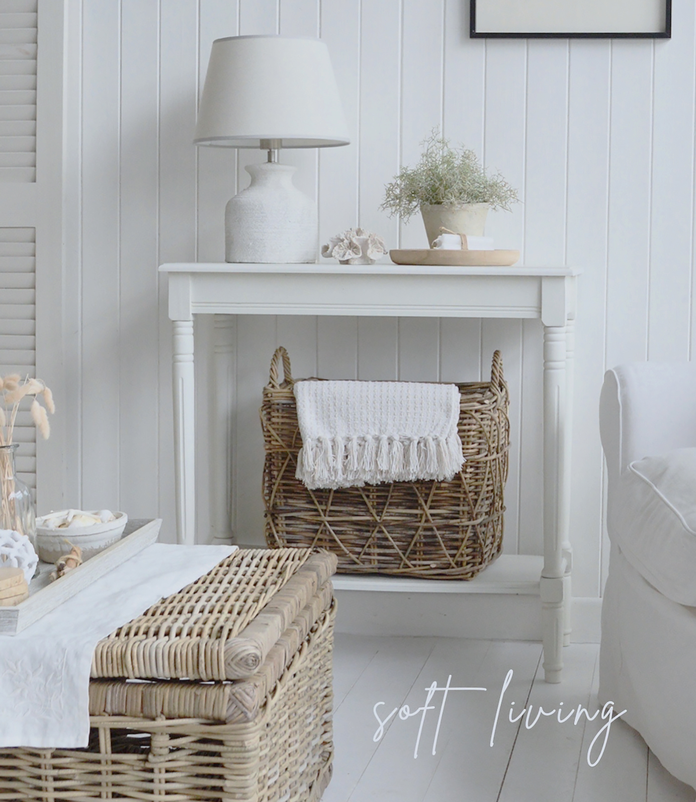A white console table, styled in a breezy coastal interior, stands gracefully against the wall with woven baskets tucked neatly underneath, blending functionality and texture while evoking a serene, beach-inspired charm that feels both inviting and timeless.