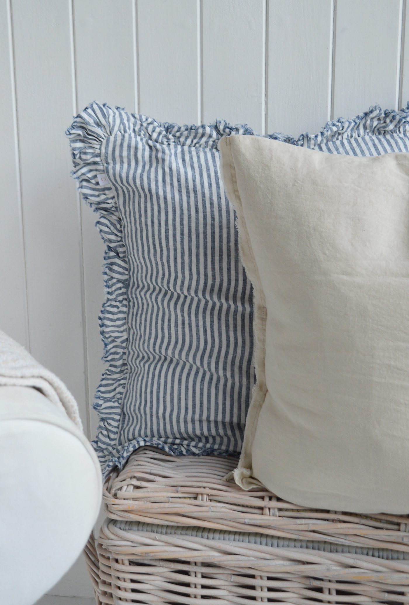 Blue and white striped ruffle cushion with neutral linen pillow on coastal rattan trunk in Hamptons-style interior