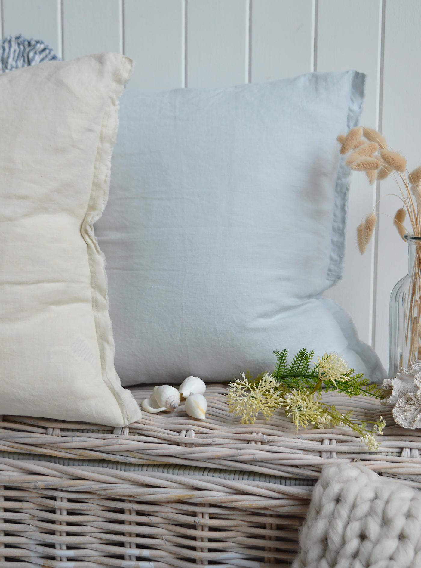 Neutral and pale blue linen cushions with seashells and native florals on whitewashed rattan trunk in Hamptons coastal interior