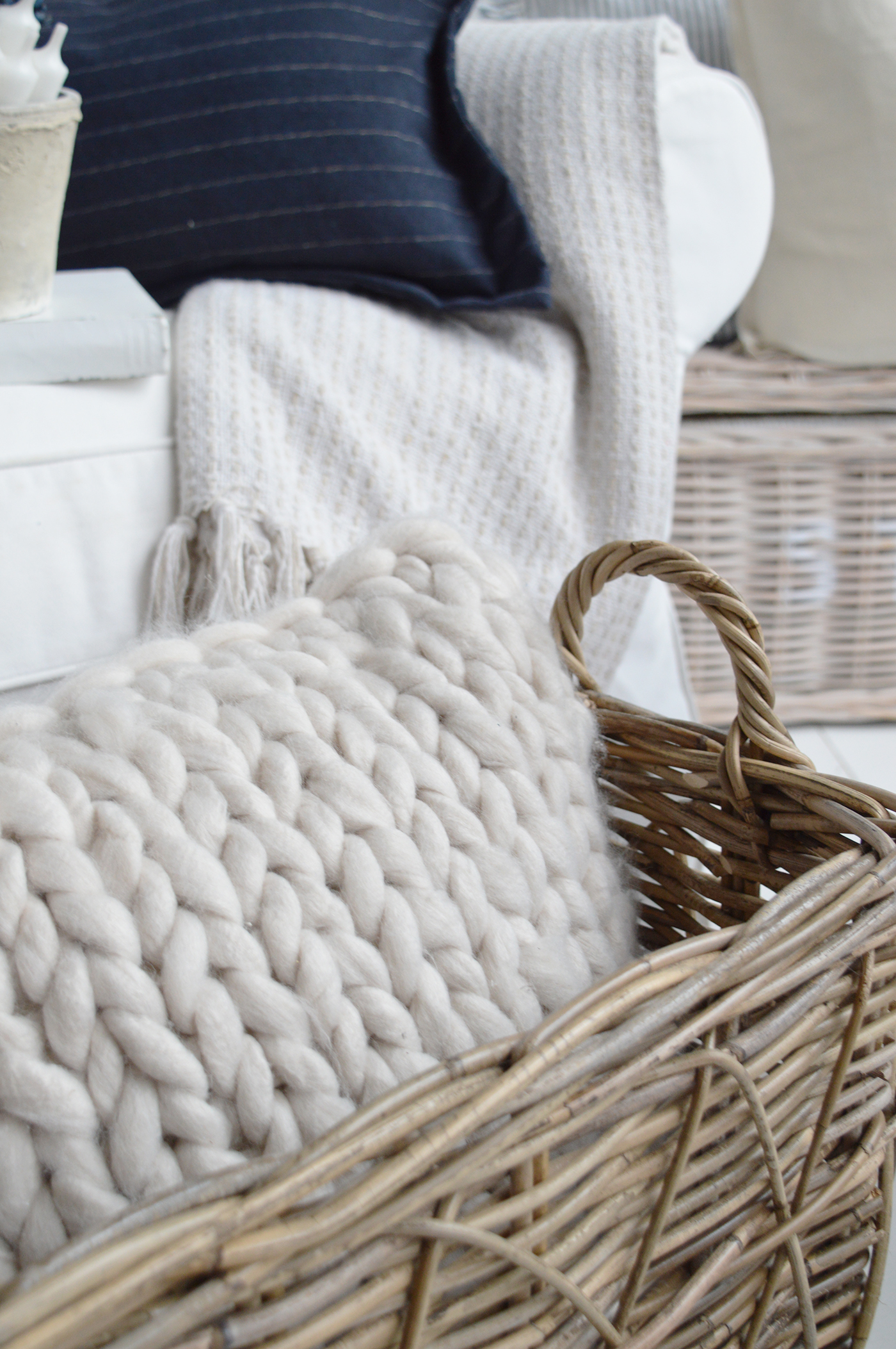 Chunky knit wool cushion in rattan basket with navy and cream throws in Hamptons coastal living room