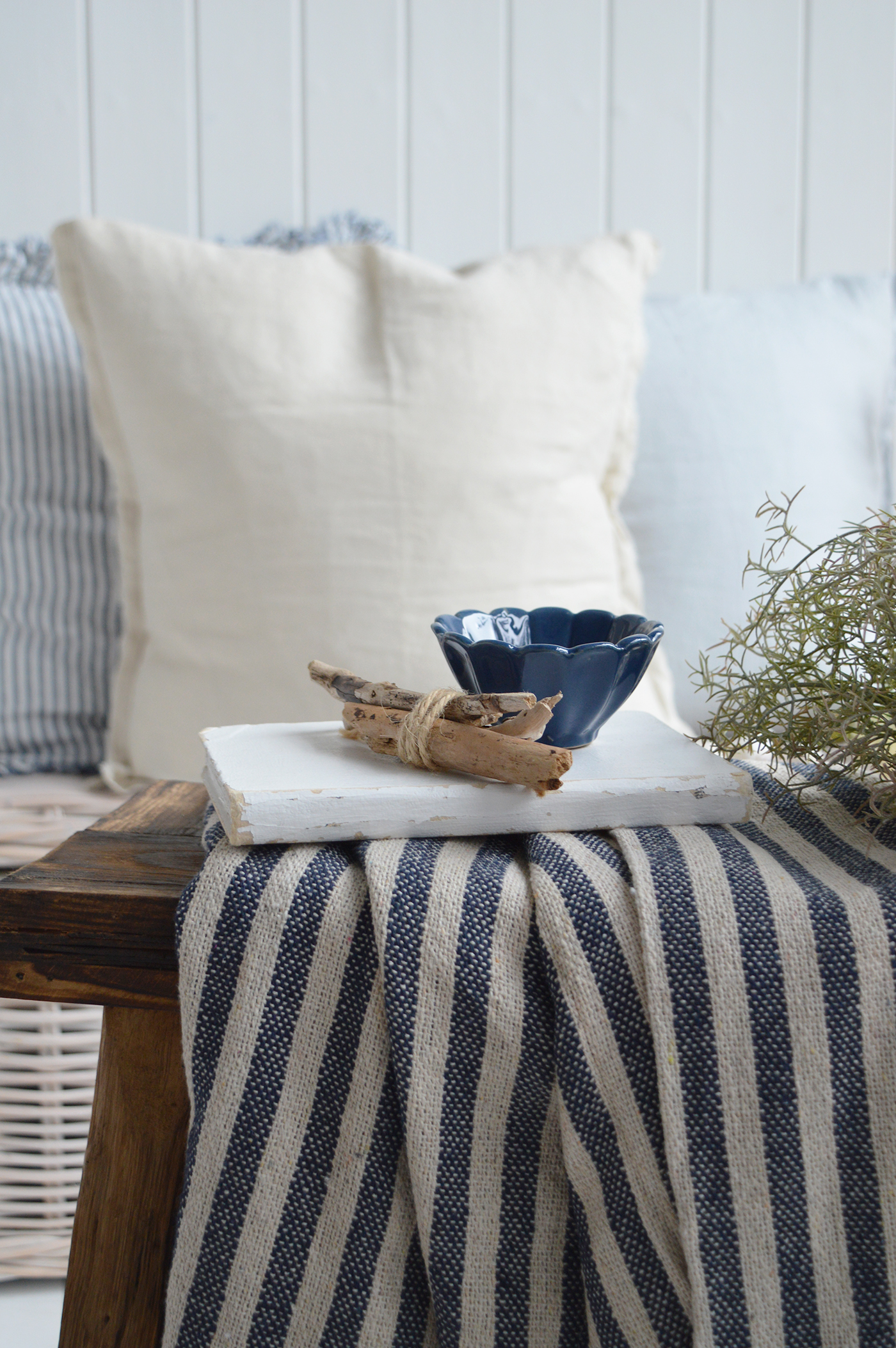 Navy scalloped bowl with driftwood on striped coastal throw in Hamptons-style beach house interior