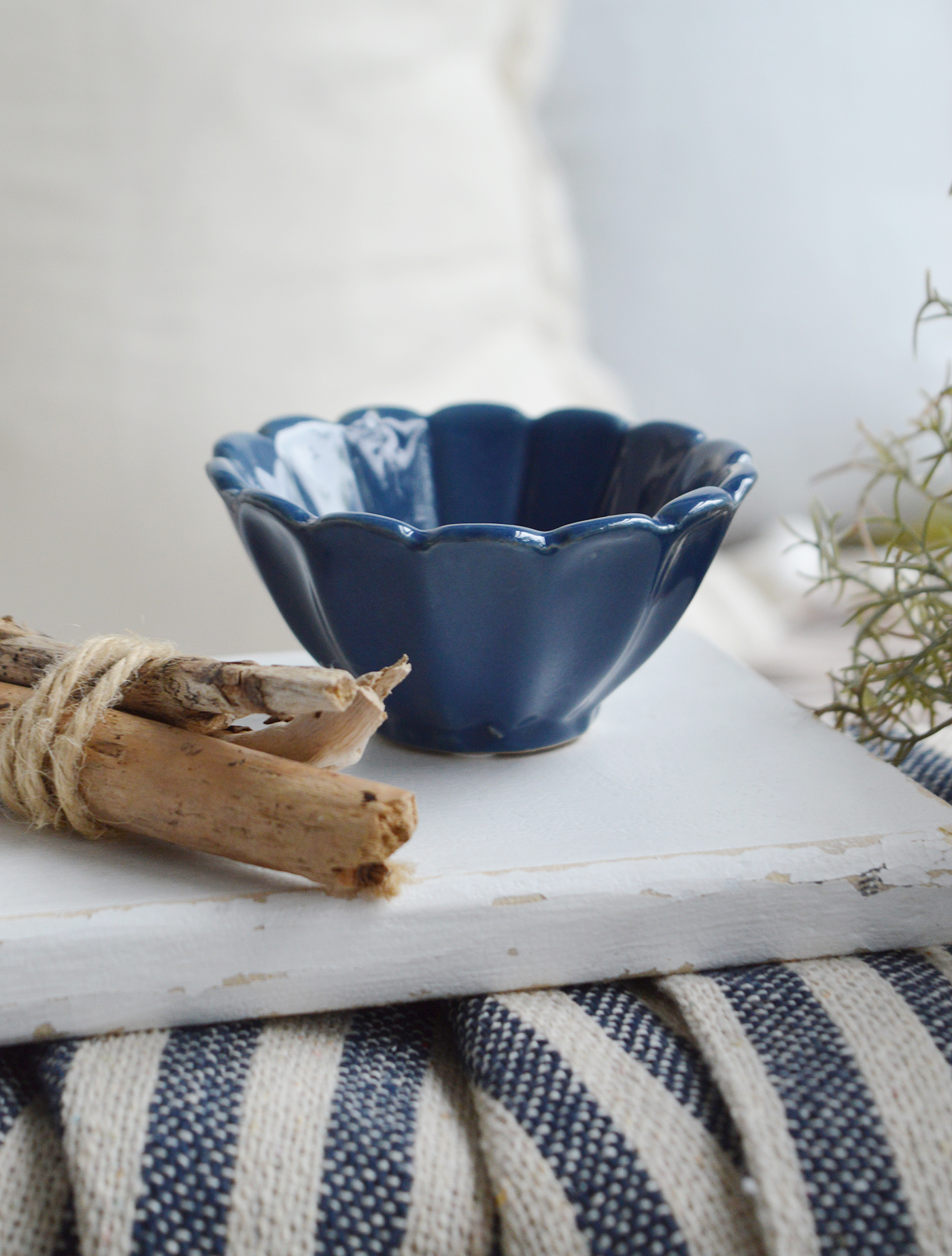Navy scalloped ceramic bowl with driftwood bundle on whitewashed board and striped Hamptons throw