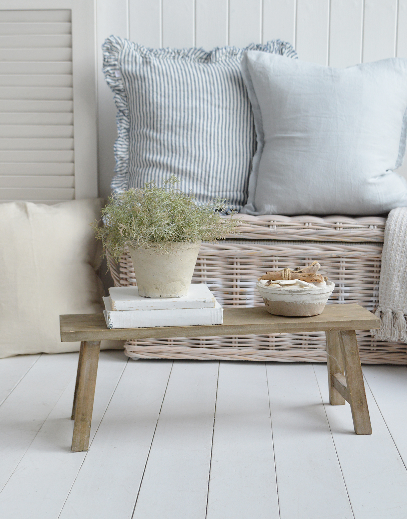 Coastal interiors styled with Hamptons-inspired cushions, a wicker chest, and rustic wooden bench in a beach house setting