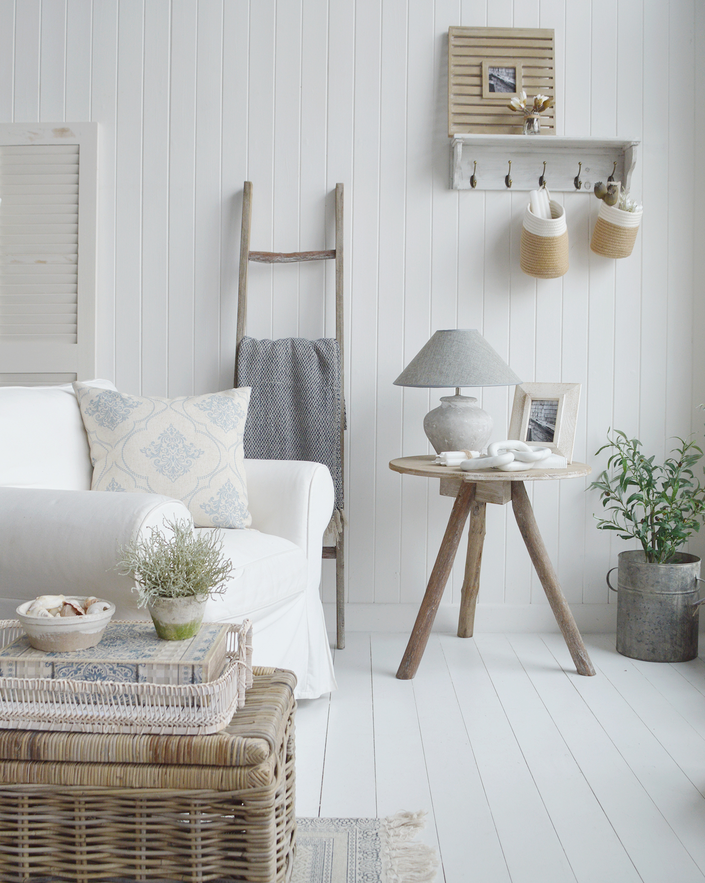 A simply styled Hamptons by the sea Living room with Coastal furniture - a driftwood side table with rattan baskets and soft blue grey cushions. A fine example of beach house interior design