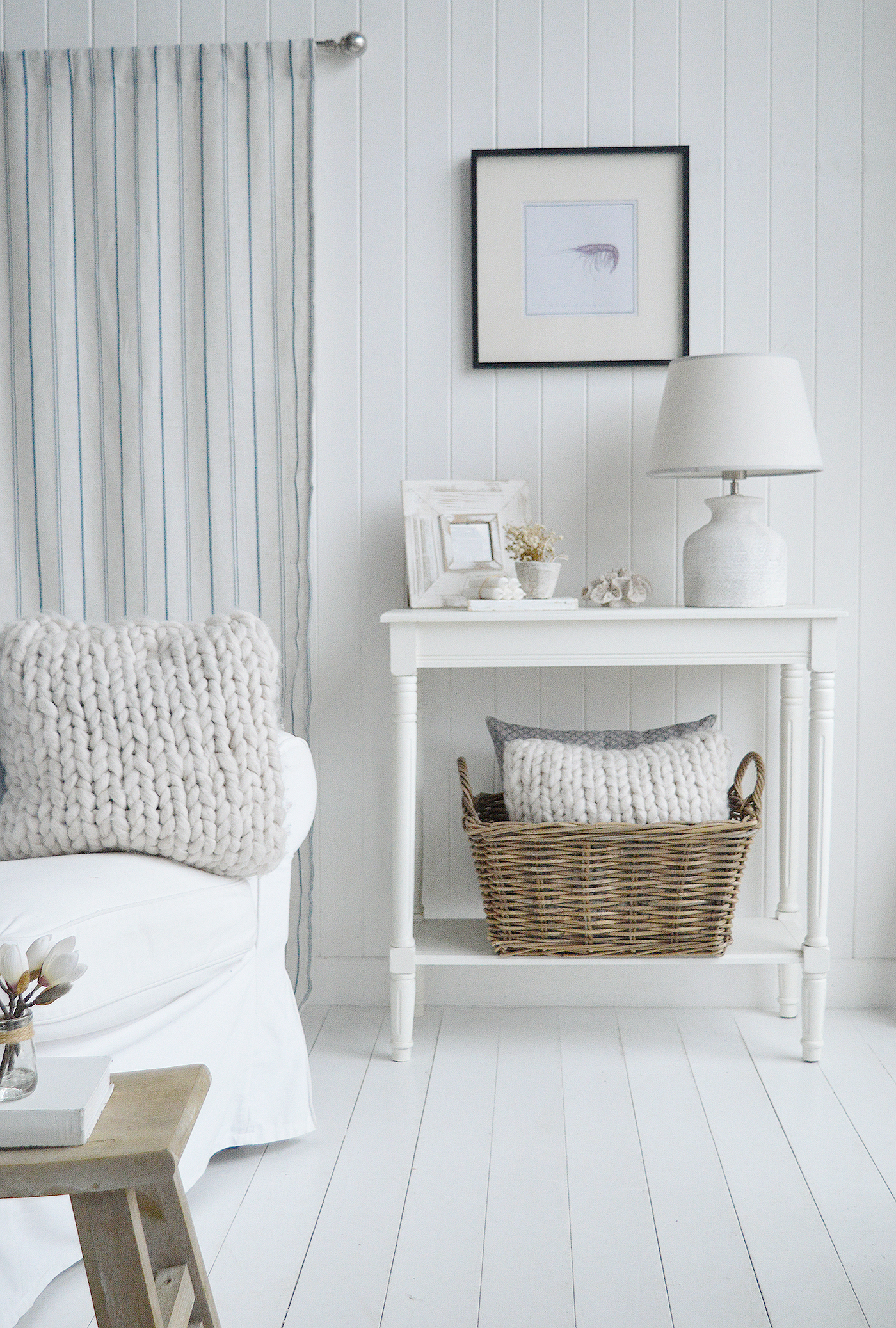 Coastal white and blue inspired living room with The White Cape Ann console , basket filled with cushions and the stripe Blue Haven Curtain