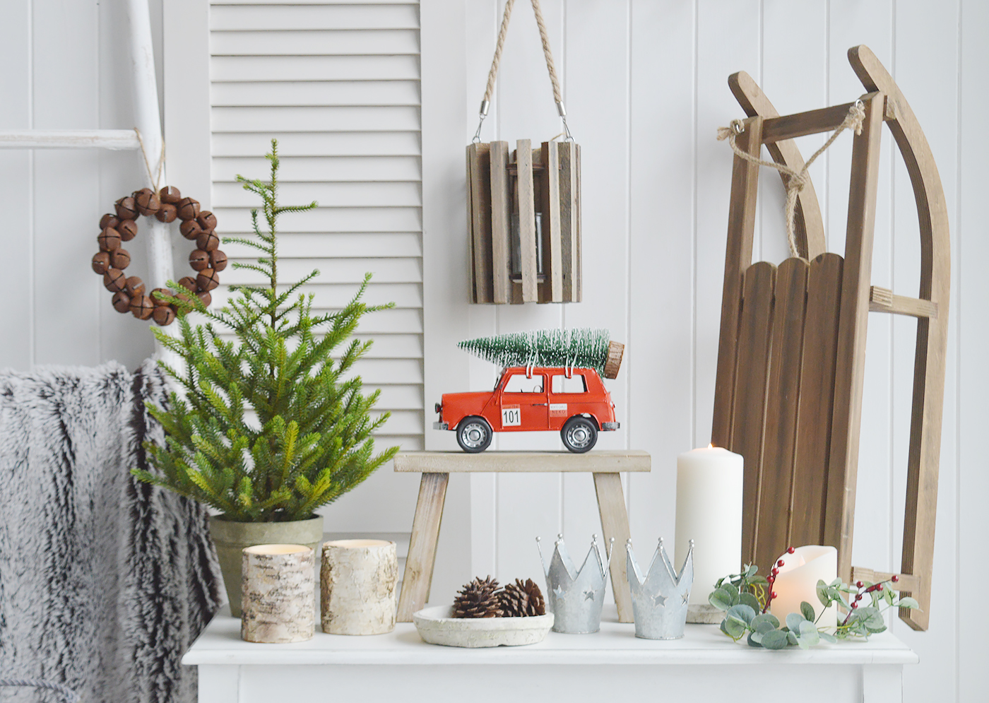 New England style Christmas decor from The White Lighthouse. Decorative wooden sleigh, red car with Christmas trees, artificial Christmas tree and festive candle holders and LED bark candles