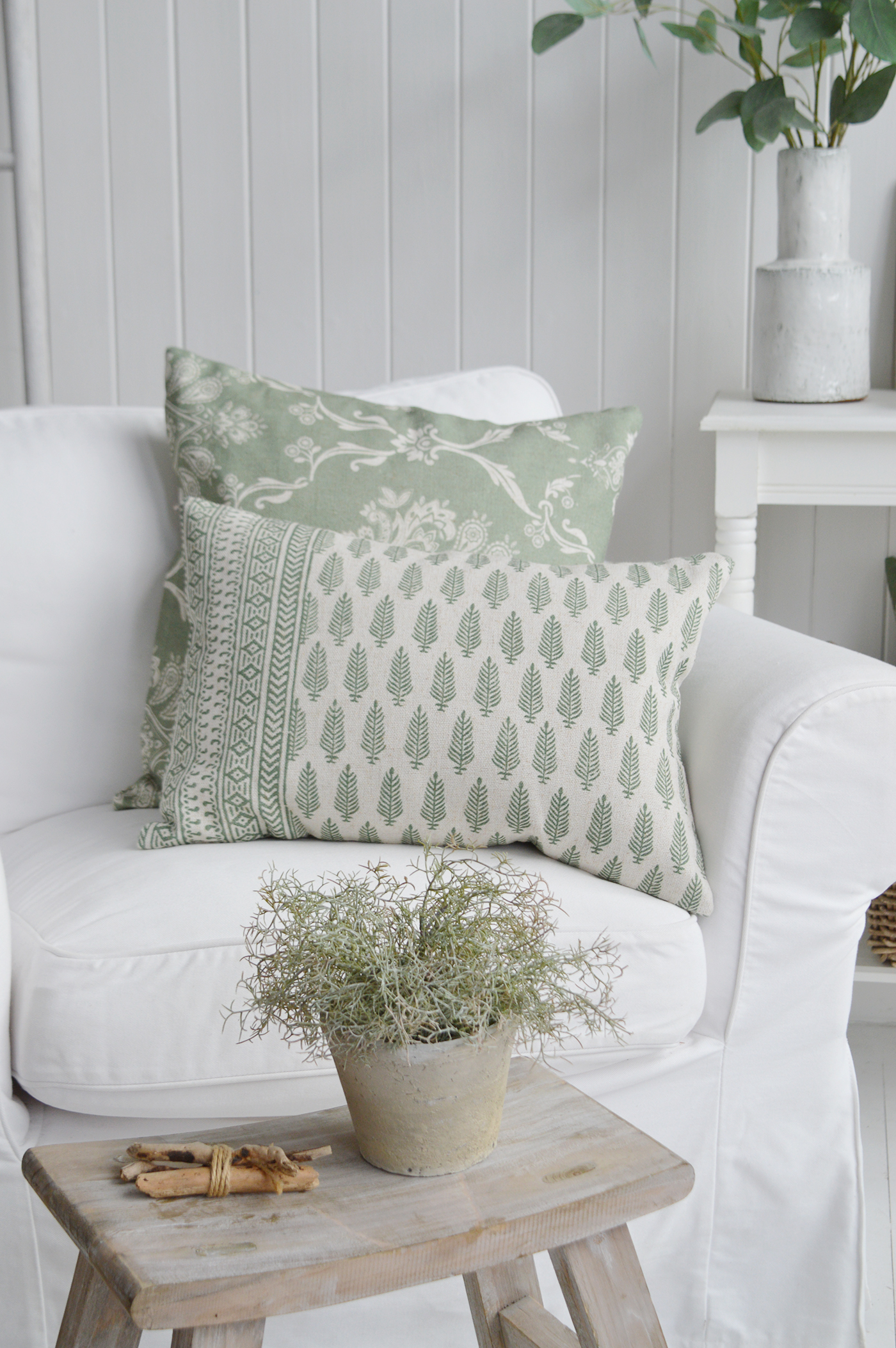 Soft sage green botanical prints bring a fresh and calming feel to this beautifully layered interior. Set against crisp white upholstery and complemented by weathered wood accents, these cushions add depth, texture and timeless charm while maintaining a light and airy coastal aesthetic. Inspired by New England interiors and relaxed country living, the combination of delicate patterns, natural tones and organic textures creates an inviting space that feels effortlessly elegant, comfortable and connected to nature.