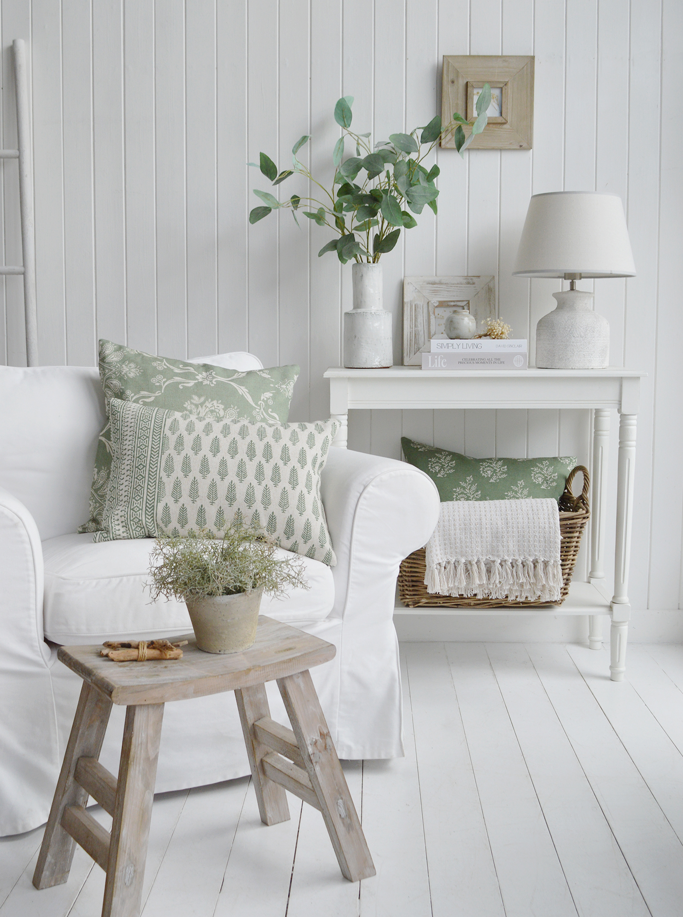 Fresh sage green accents, weathered wood finishes and crisp white furnishings come together to create a beautifully relaxed coastal living space. Layered with natural textures, soft botanical patterns and timeless New England-inspired styling, this serene interior captures the effortless charm of coastal interiors while bringing warmth, character and a sense of calm to the home. The combination of muted greens, woven baskets, textured fabrics and light-reflecting whites creates an inviting retreat that feels both elegant and comfortably lived in.