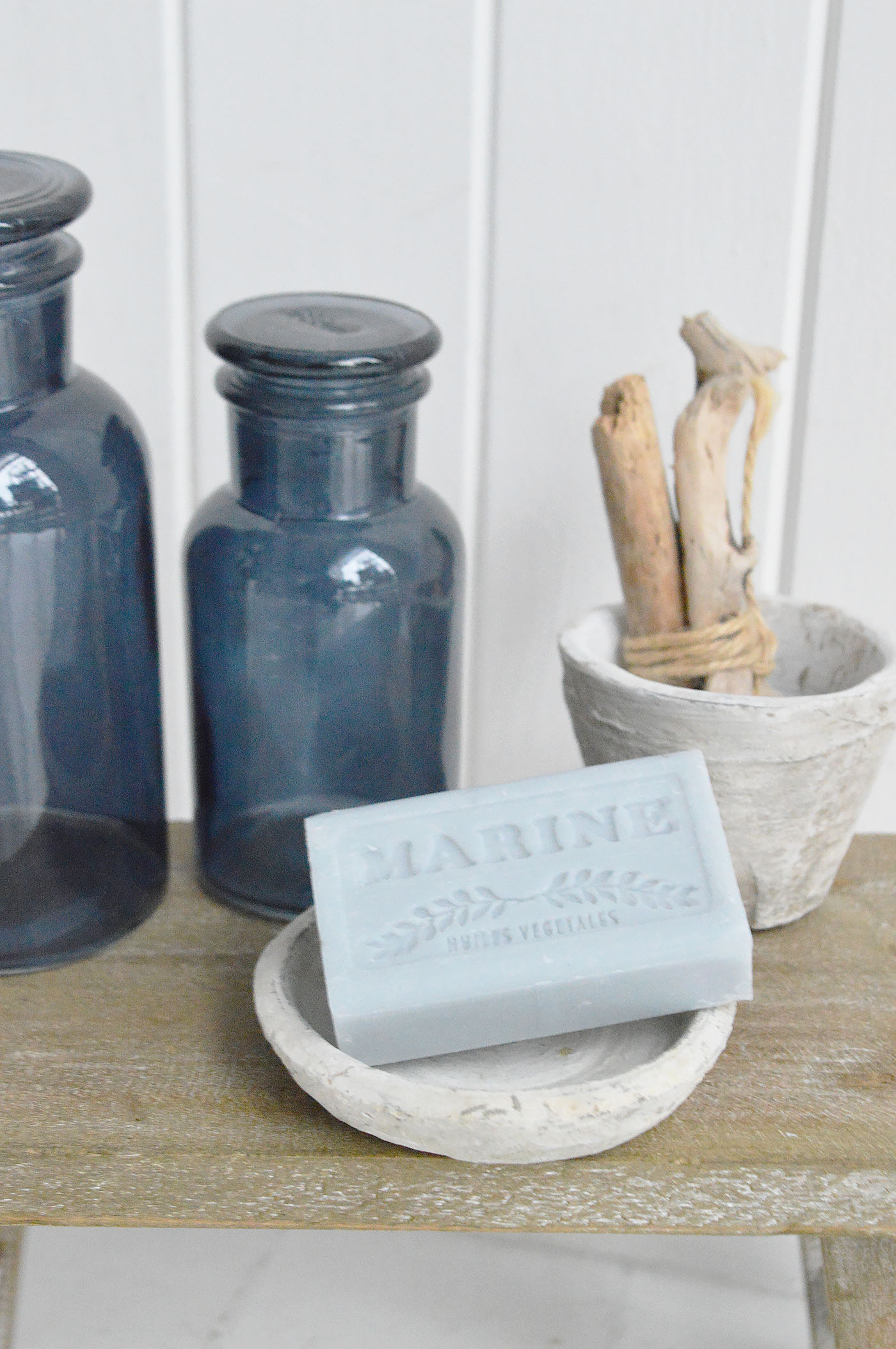 This coastal inspired styling with blue glass bottles, rustic stone accessories and a marine scented soap captures the relaxed charm of New England beach house décor, blending soft neutrals, natural textures and timeless coastal accents.