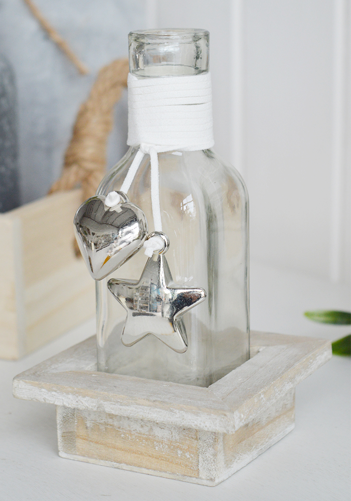 A decorative square bottle with a hanging silver mirrored chunky heart and star in a driftwood style wooden crate