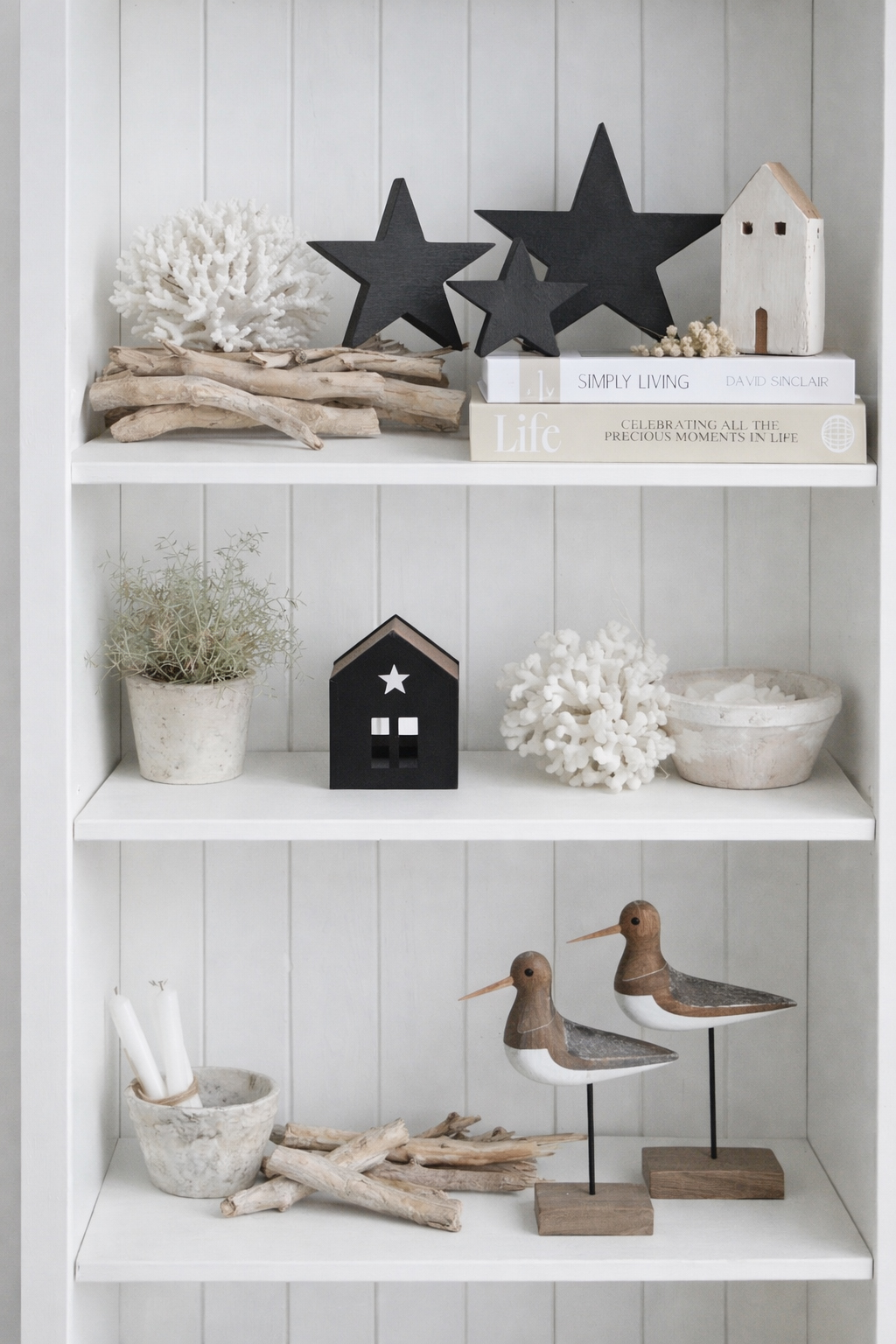 Styled in a relaxed New England coastal interior, this white bookcase features layered neutral tones with natural driftwood, sculptural coral, decorative houses and wooden black stars, creating a beautifully balanced display that captures the calm, textural feel of coastal living.