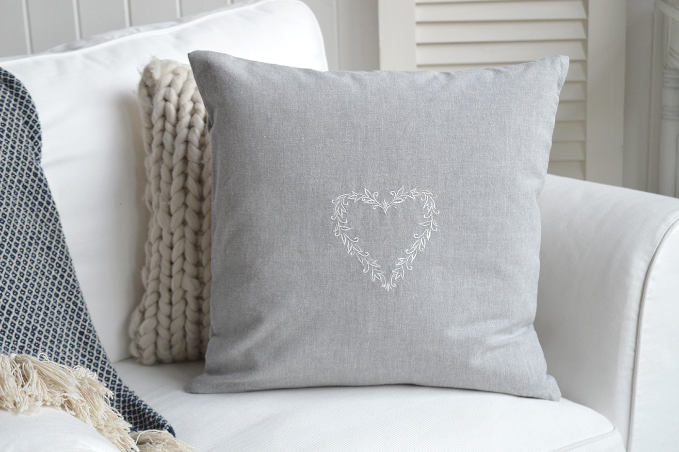 Grey cushion with white embroidered heart on neutral sofa in coastal living room