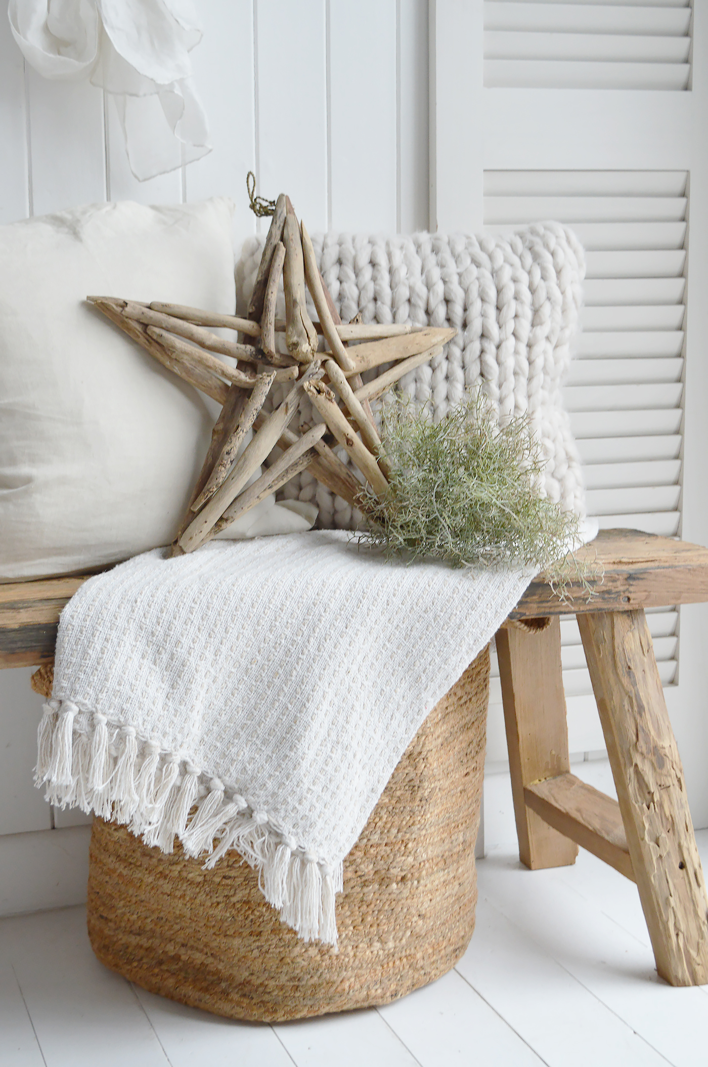 A coastal inspired wooden bench layered with driftwood stars, cushions, throws and spanish moss