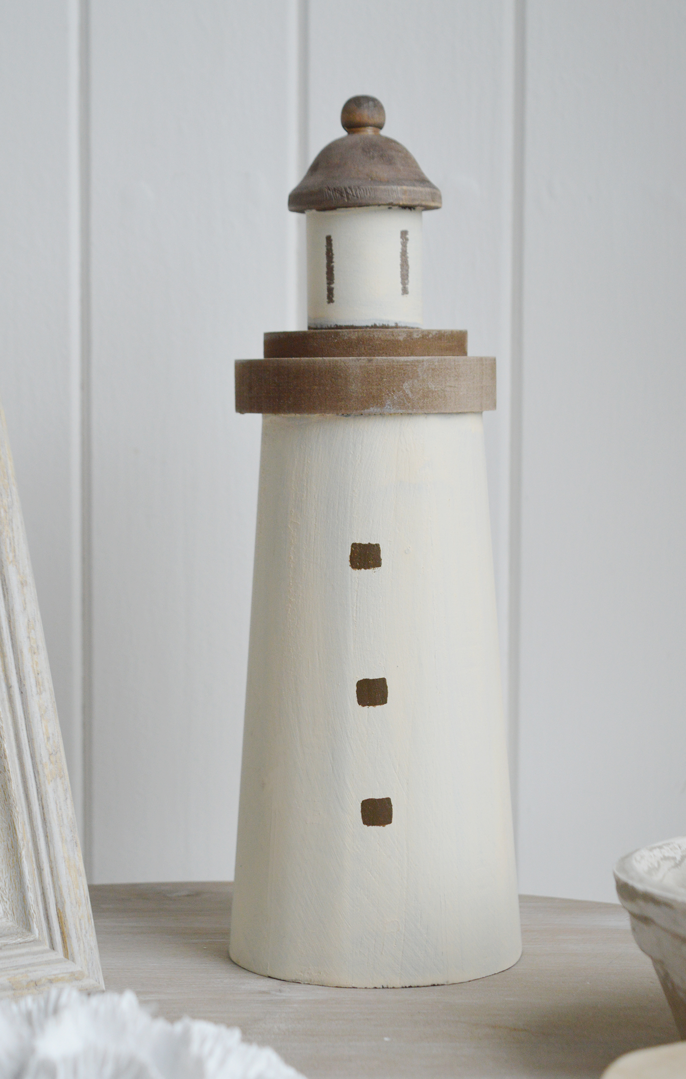 A decorative wooden lighthouse. A charming piece of beach house decor evoking a rustic coastal vibe, with a weathered painted finish to give the impression it has been aged by sea breezes and salt air for a timeless seaside aestheti