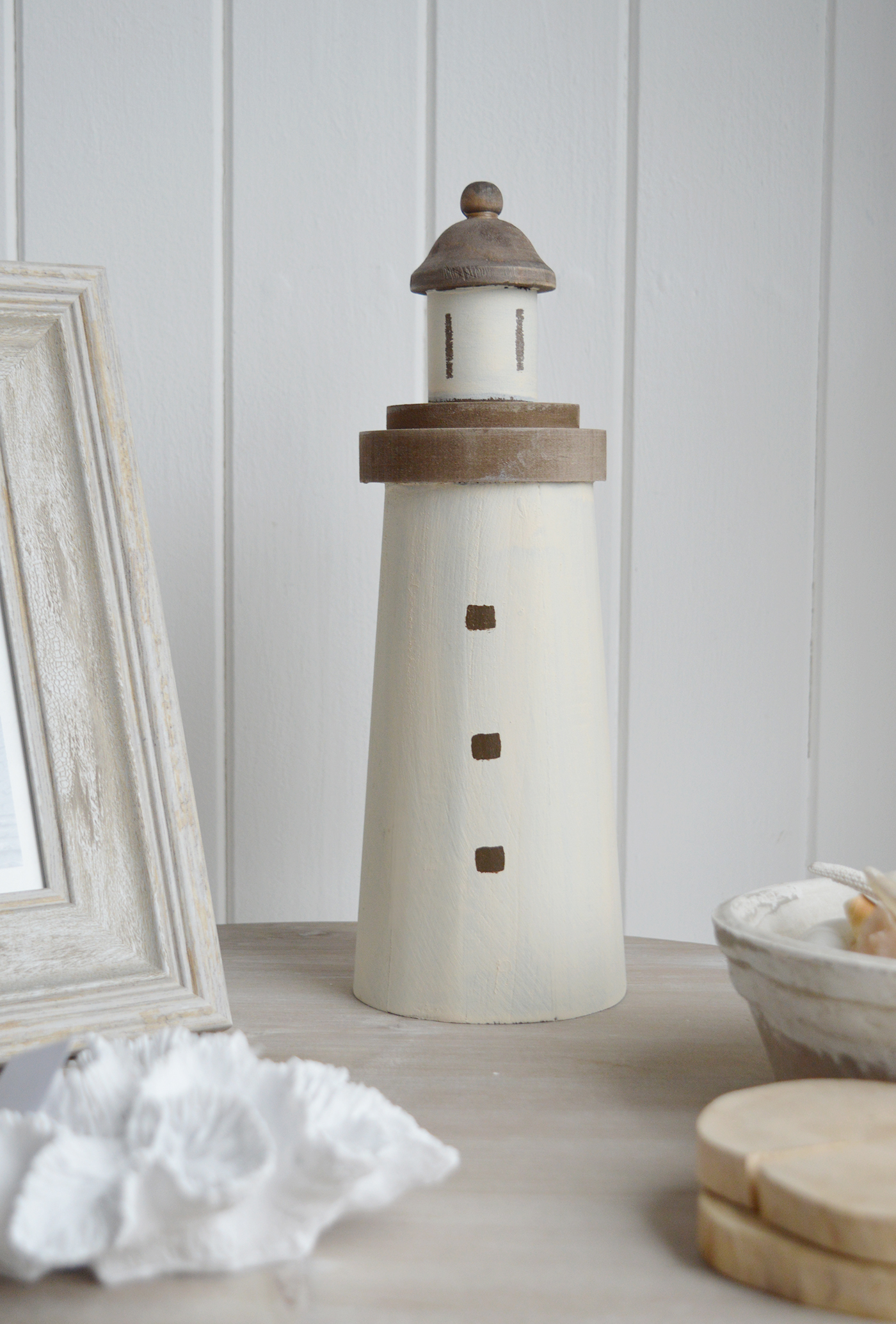 A decorative wooden lighthouse. A charming piece of beach house decor evoking a rustic coastal vibe, with a weathered painted finish to give the impression it has been aged by sea breezes and salt air for a timeless seaside aestheti