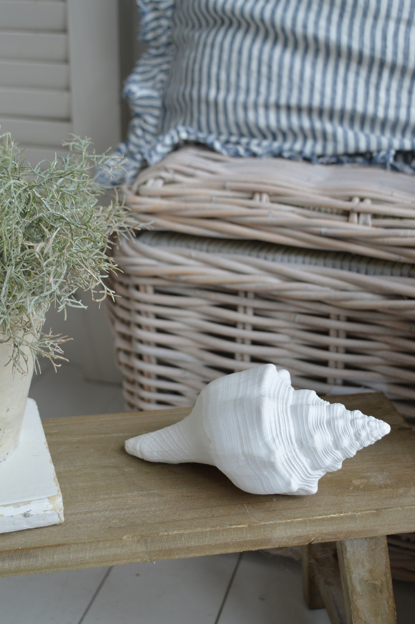 White resin conch shell decor on a rattan console table with nautical accents and soft blue tones
