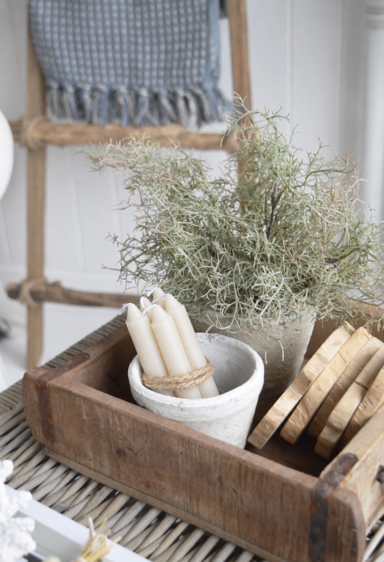 Create a coastal coffee table display with faux greenery, white candles and natural wooden coasters.