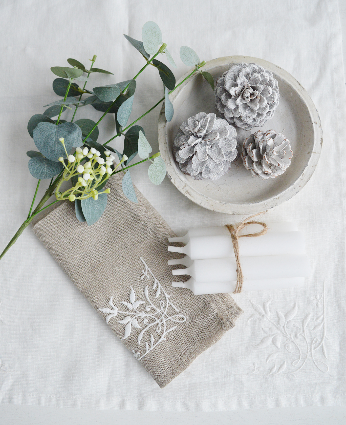 Festive Table decfor with white linen table runner, linen, napkin, candles, Eucalyptus Sprif and pinecones