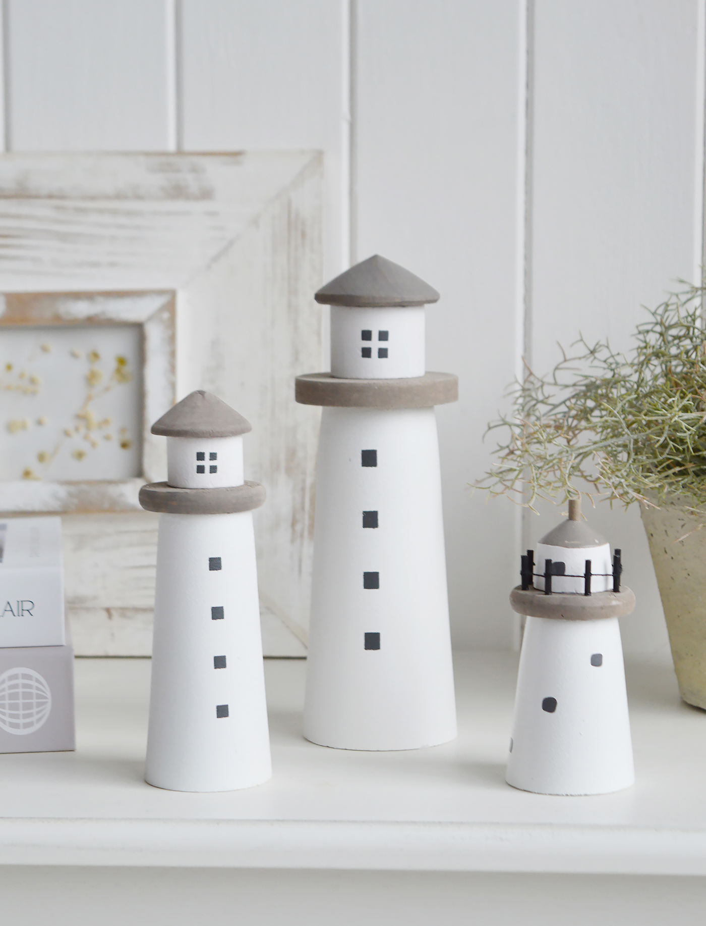 A decorative wooden lighthouse. A charming piece of beach house decor evoking a rustic coastal vibe, with a weathered painted finish to give the impression it has been aged by sea breezes and salt air for a timeless seaside aestheti