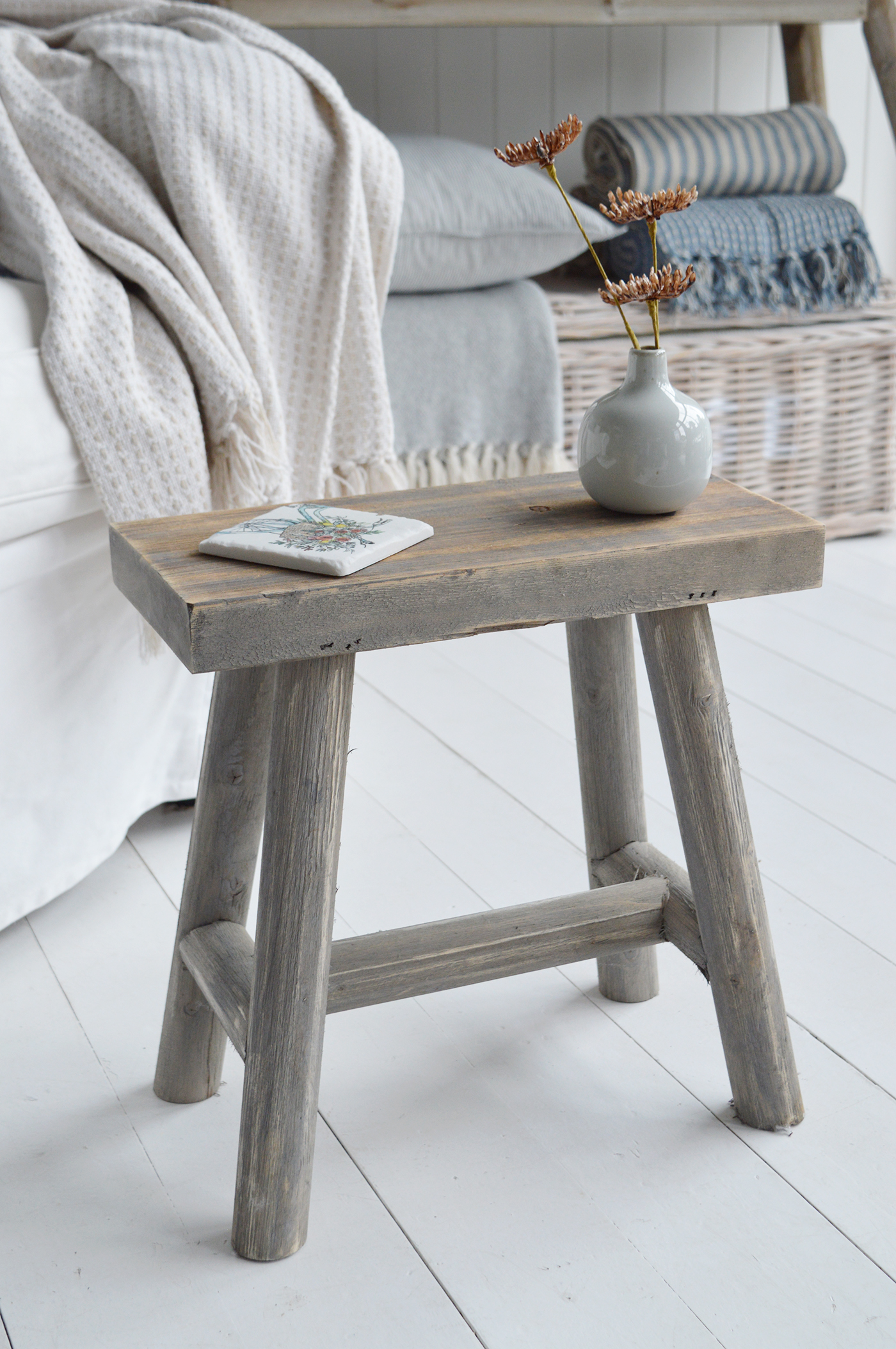 Modern country interiors with rustic stool, ceramic vase, striped blankets, and coastal chic Hamptons details