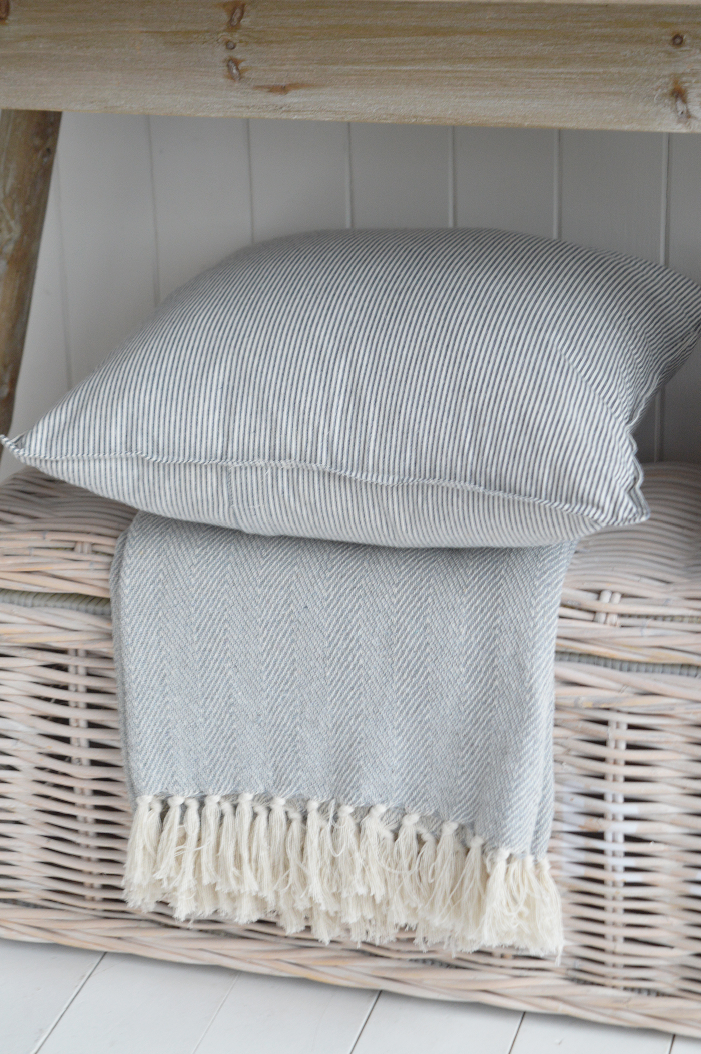 Modern country interiors with striped cushion, fringed throw, and wicker trunk in coastal chic Hamptons style