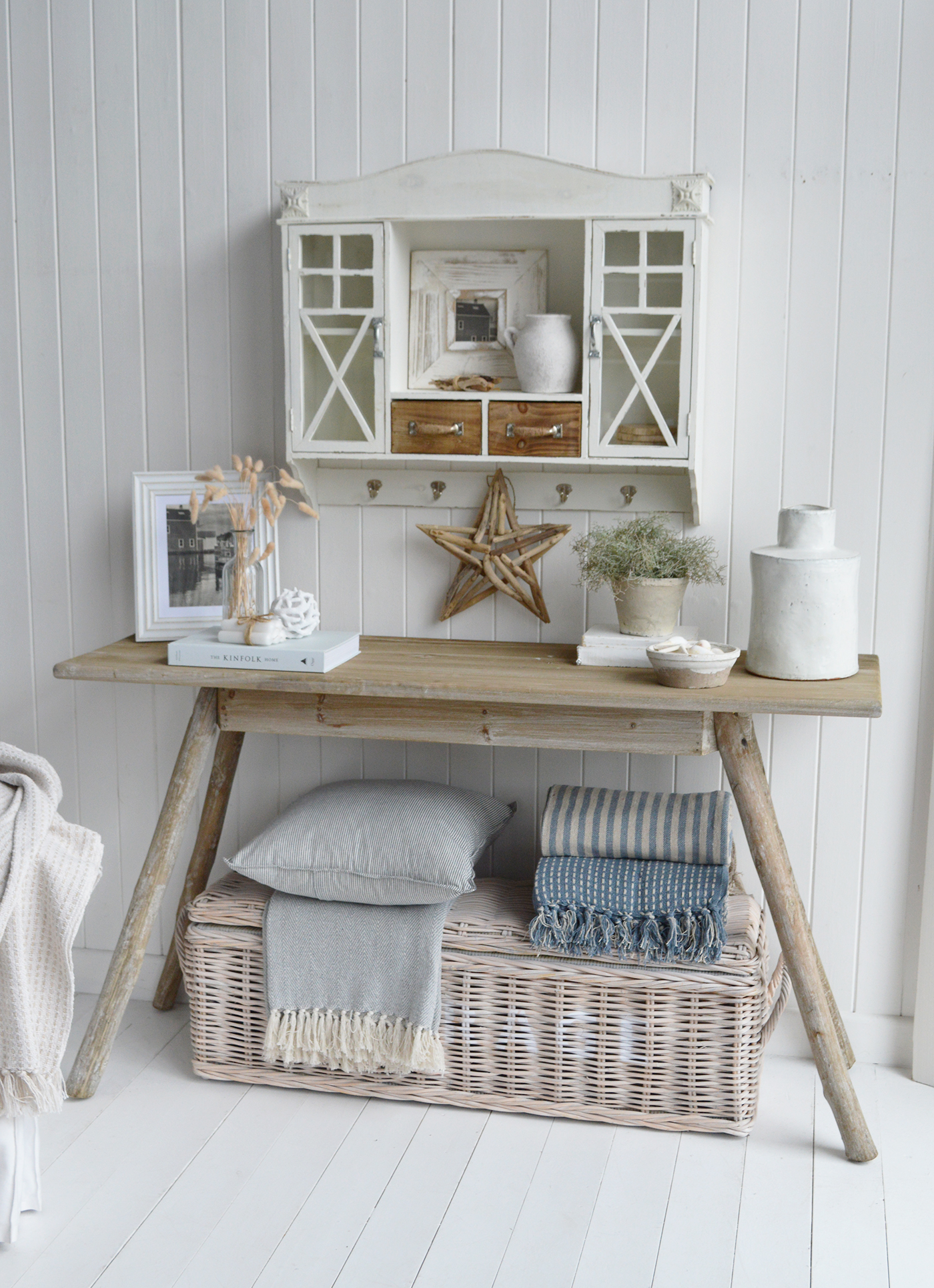 Modern country interiors with rustic console, wicker basket, striped throws, and coastal chic Hamptons accents.
