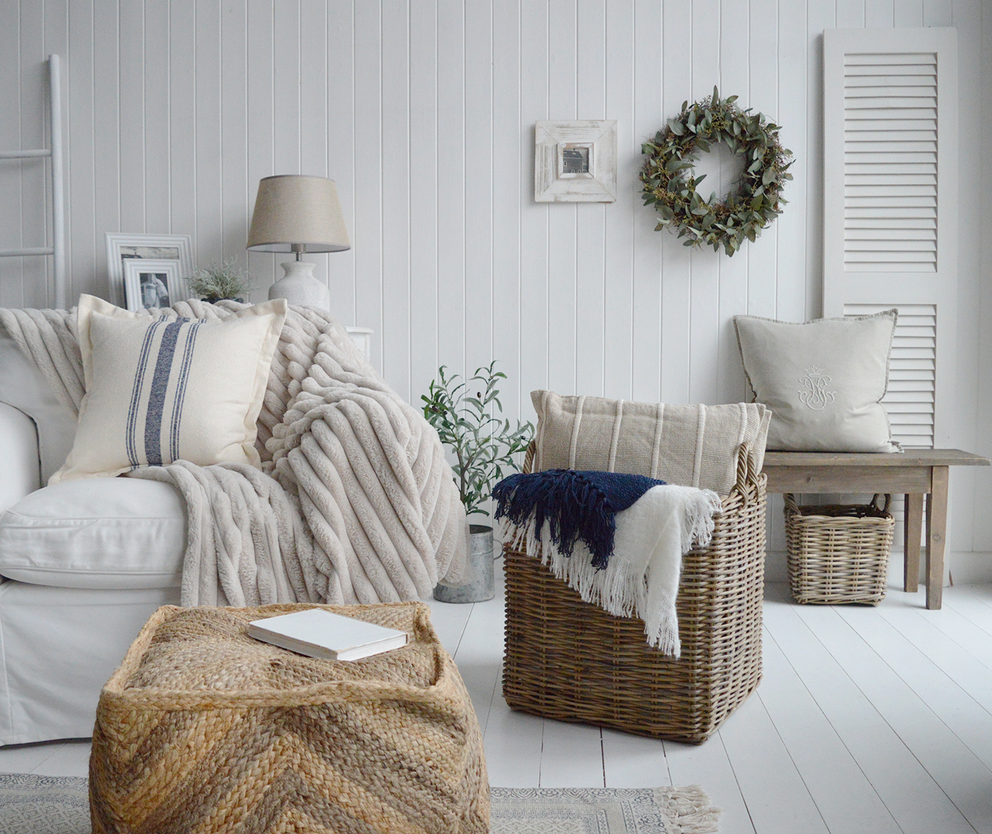 A New England coastal and modern country farmhouse living room, how to decorate and style with furniture and accessories using layers as the basis on interior design. Showing the Benton Pouffe, large log basket filled with cushions, blankets and throws and the Pawtucket bench at the back