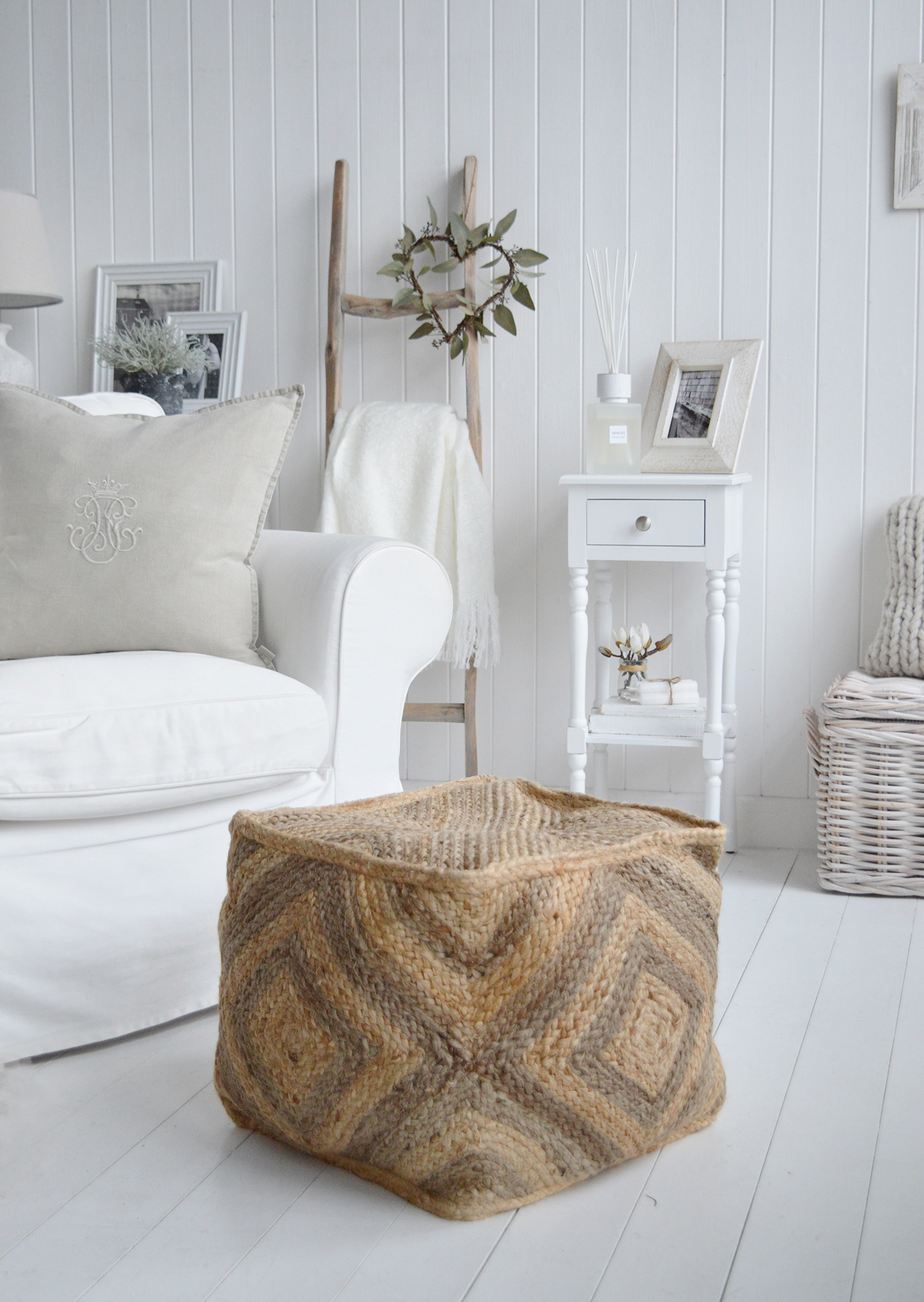 The Benton footstool in a white living room with touches of warmth from the driftwood ladder and cushions. Includes the white narrow Georgetown lamp table with a drawer and shelf