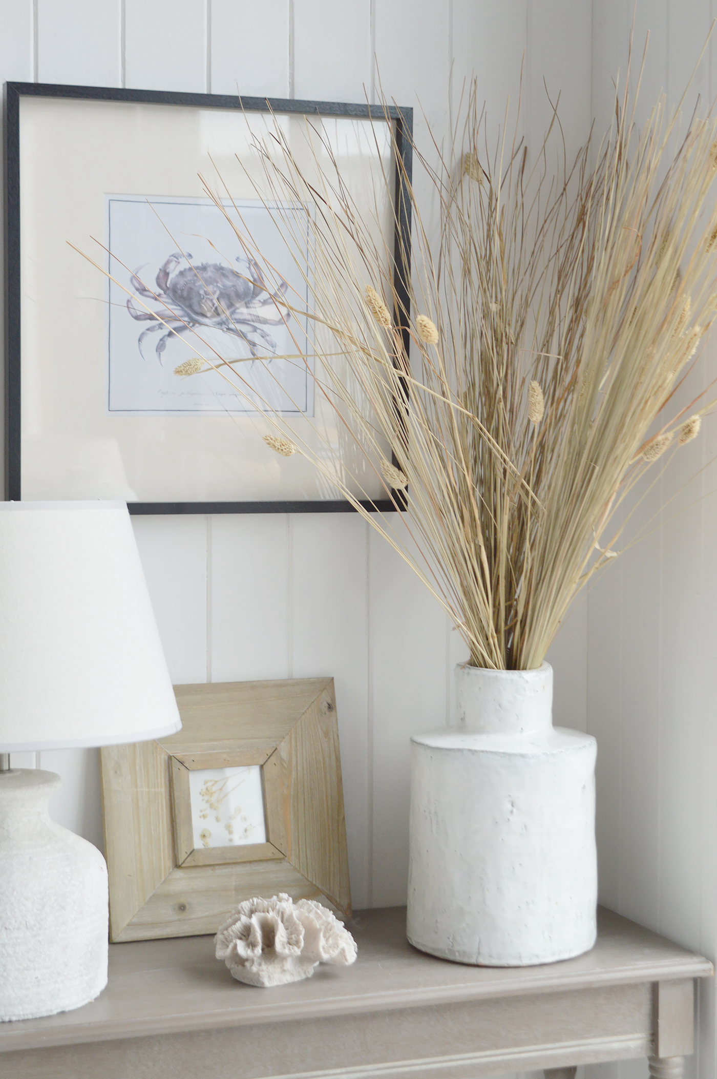 Dried grasses in a textured white vase, pale wood frames and a coral ornament bring natural texture to this neutral coastal living room, creating a relaxed New England feel.