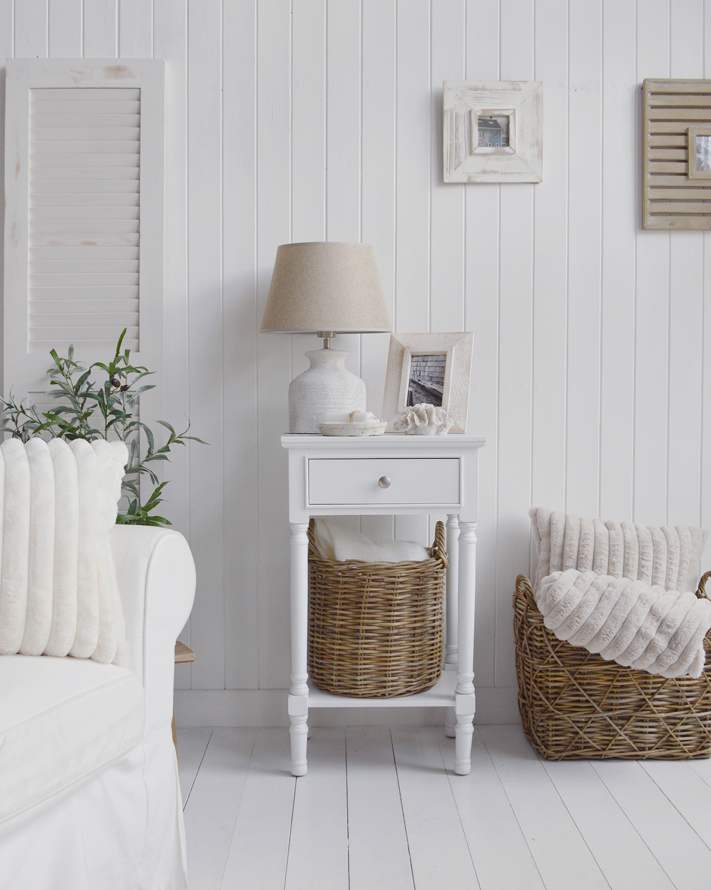 The Georgetown white lamp table, ideal as a bedside with a drawer and shelf... shown here in a white beach house interiors with baskets and cosy throws and cushions adding warmth