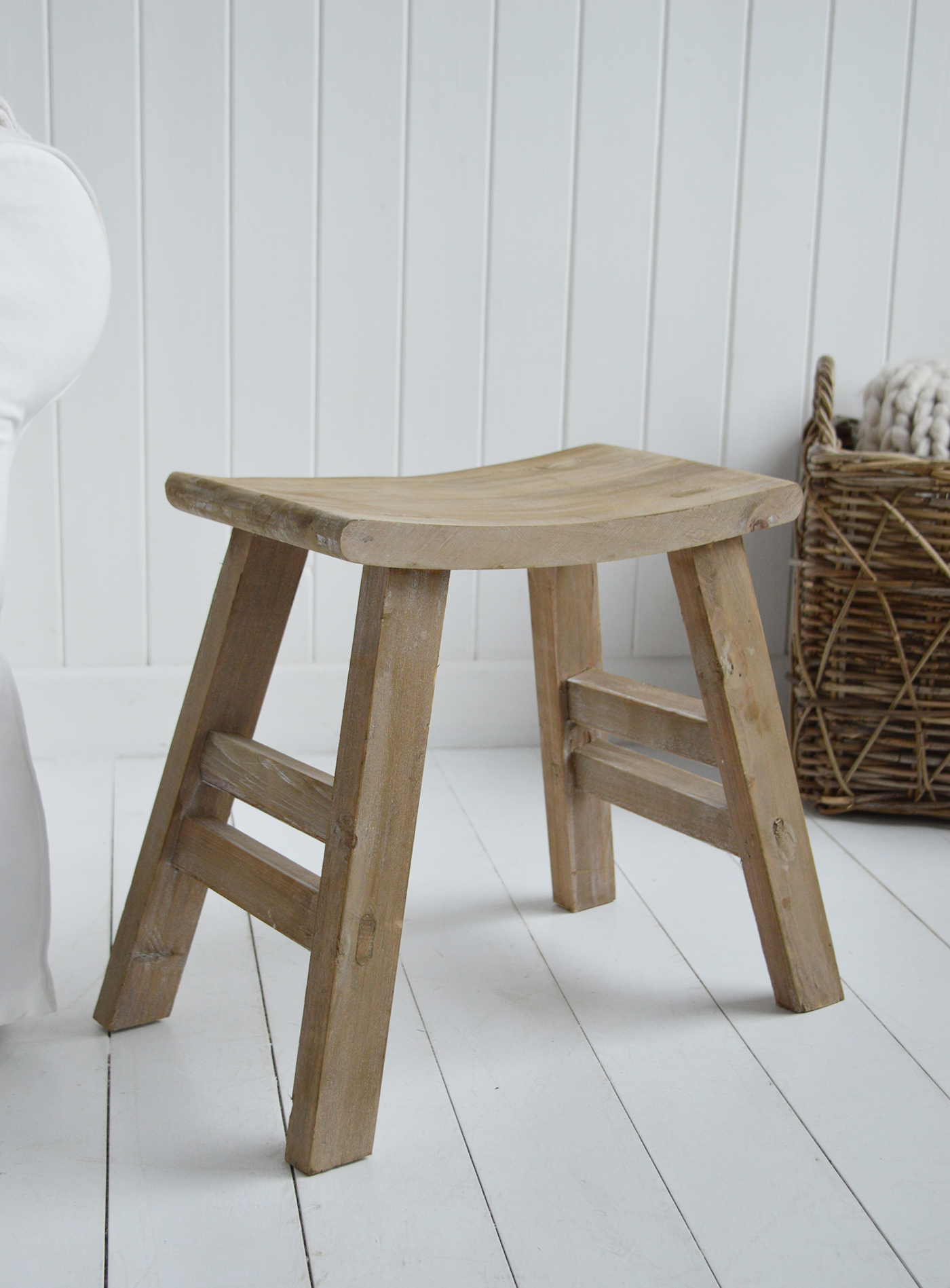Versatile Pawtucket wooden accent stool styled as side table with plant and books. Curved top wooden stool against white shiplap wall in coastal interior setting