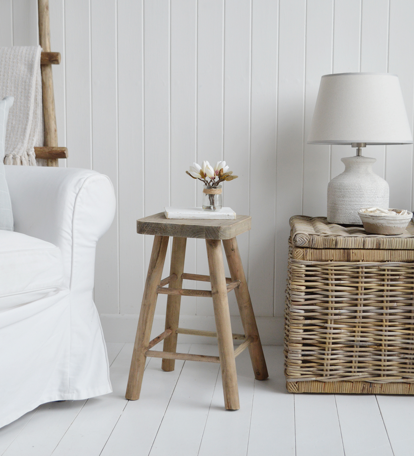 The sturdy wooden stool, repurposed as a table, stands beside the open window, catching the ocean breeze that drifts through the beach house. Its weathered surface holds a lantern and a dog-eared novel, perfect for quiet seaside evenings.