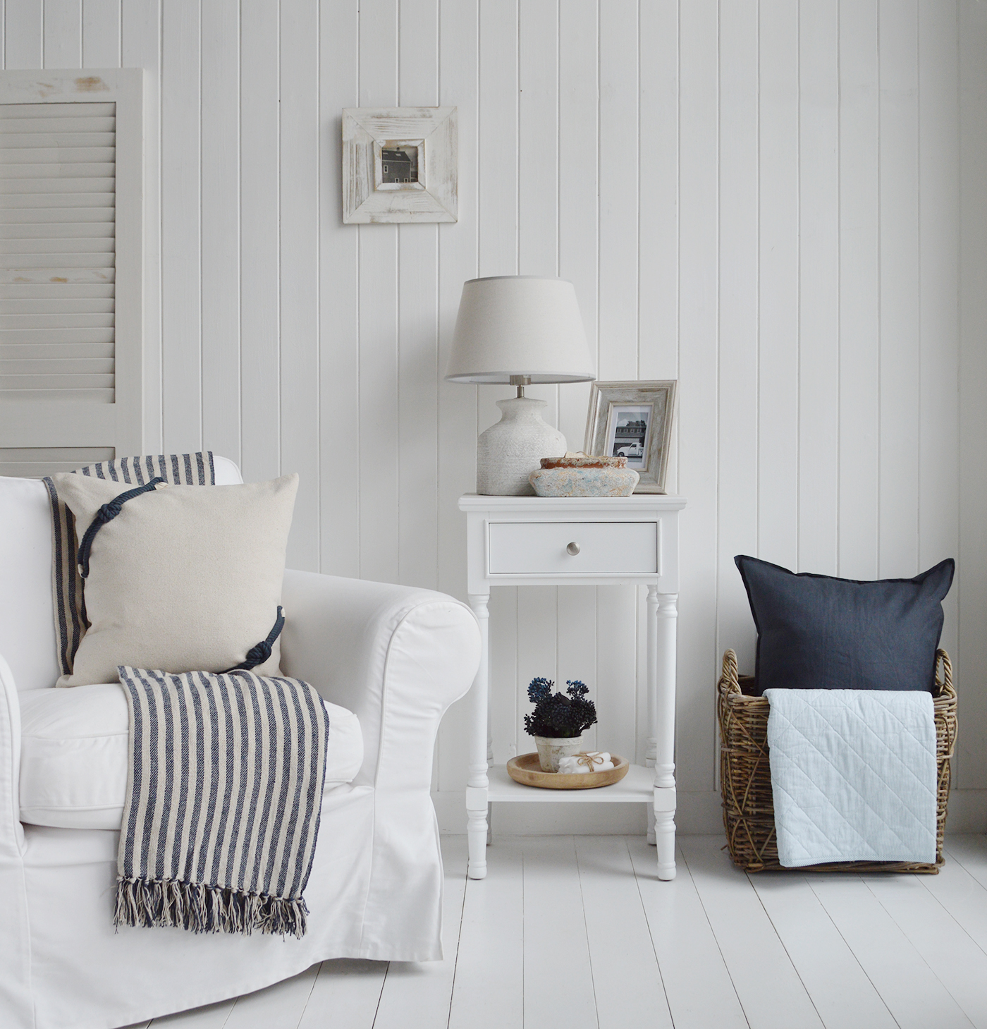 Coastal style cushion and navy and natural stripe throw styled with a white lamp table in a light, beach-inspired New England blue and white interior
