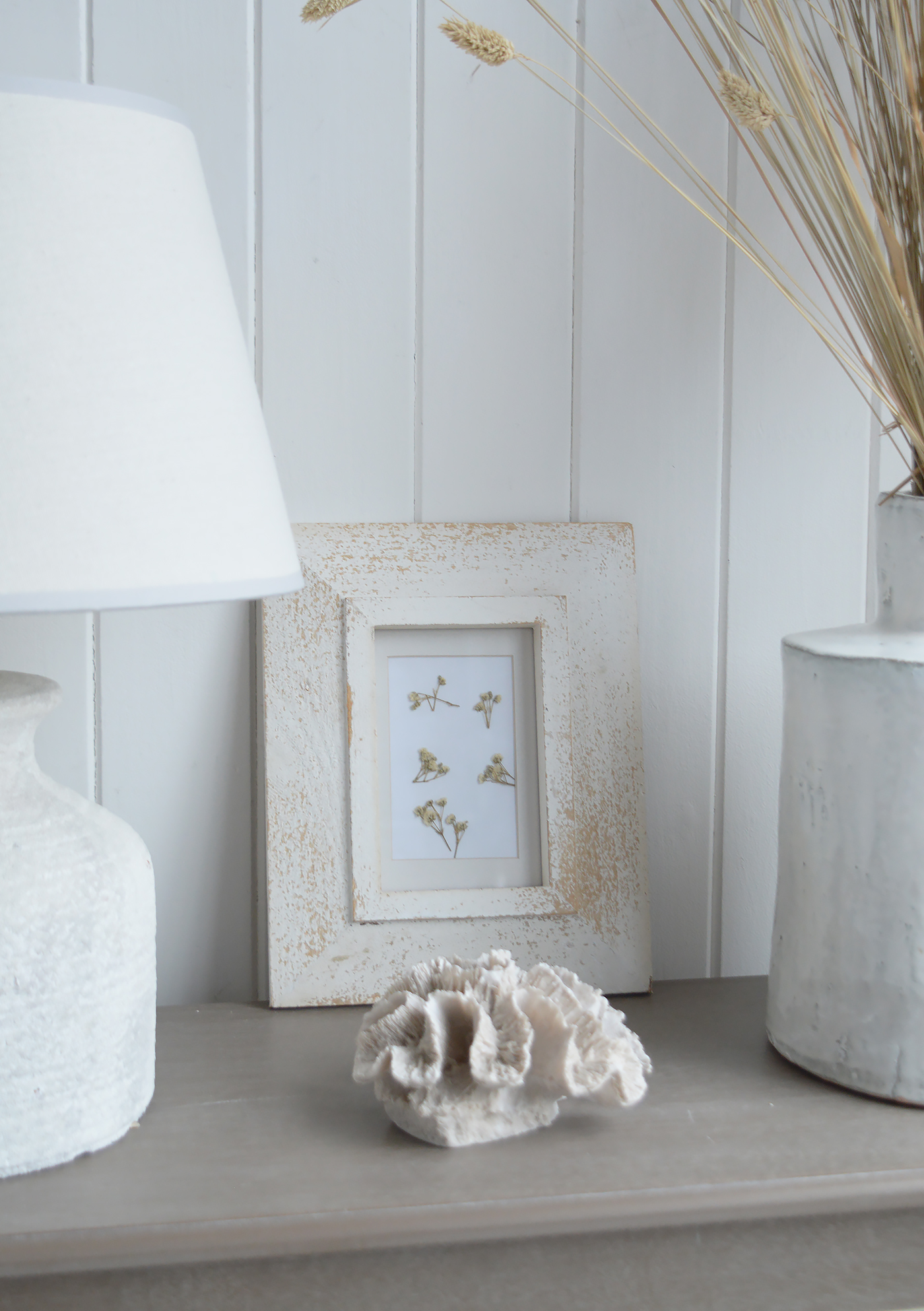 White accessories, dried grasses and a decorative shell create a soft, neutral display on greywashed furniture, ideal for modern coastal interiors.