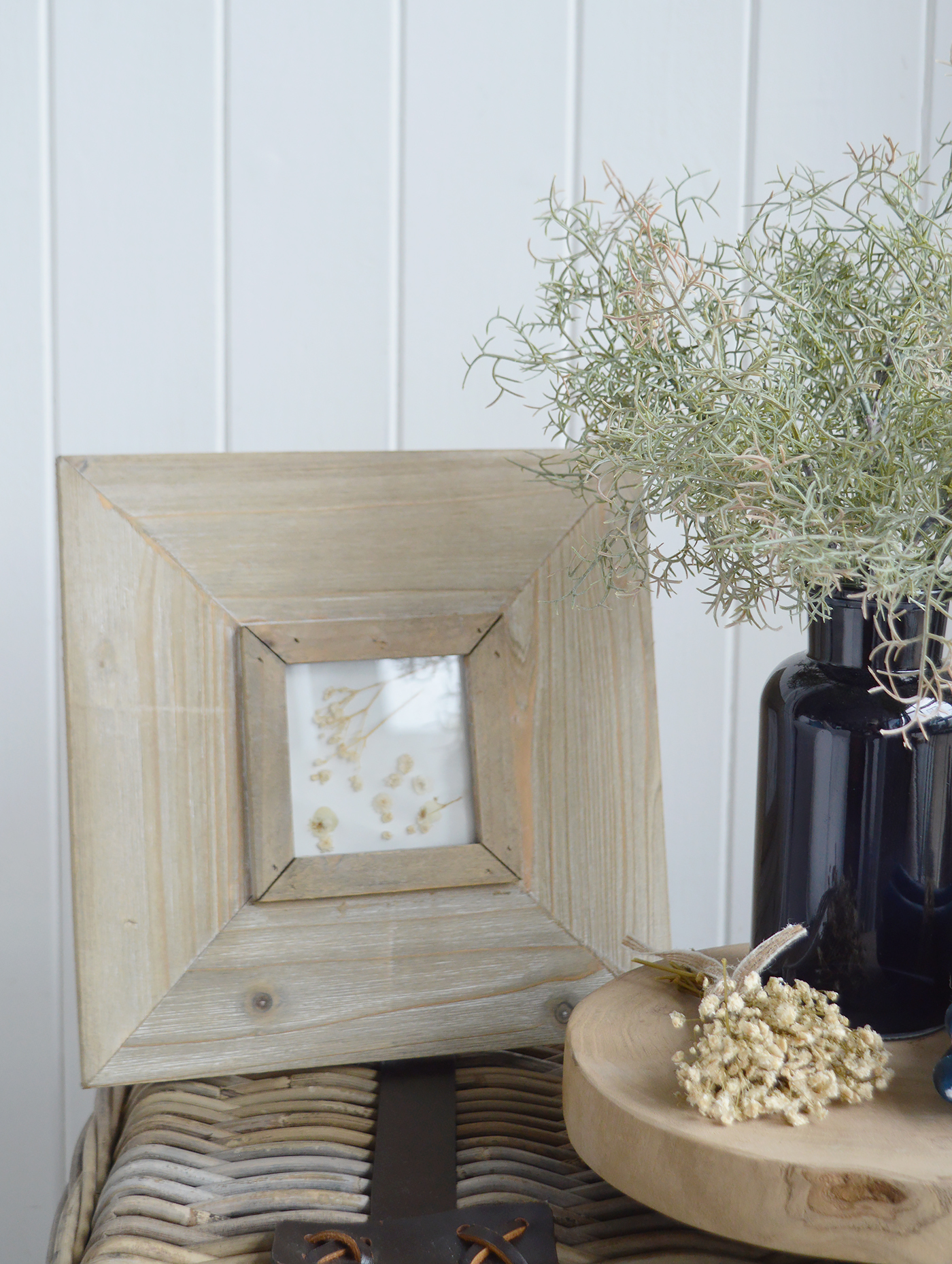 A weathered wooden frame, navy vase and soft greenery bring texture and depth to modern coastal interiors, complementing natural woven furniture.