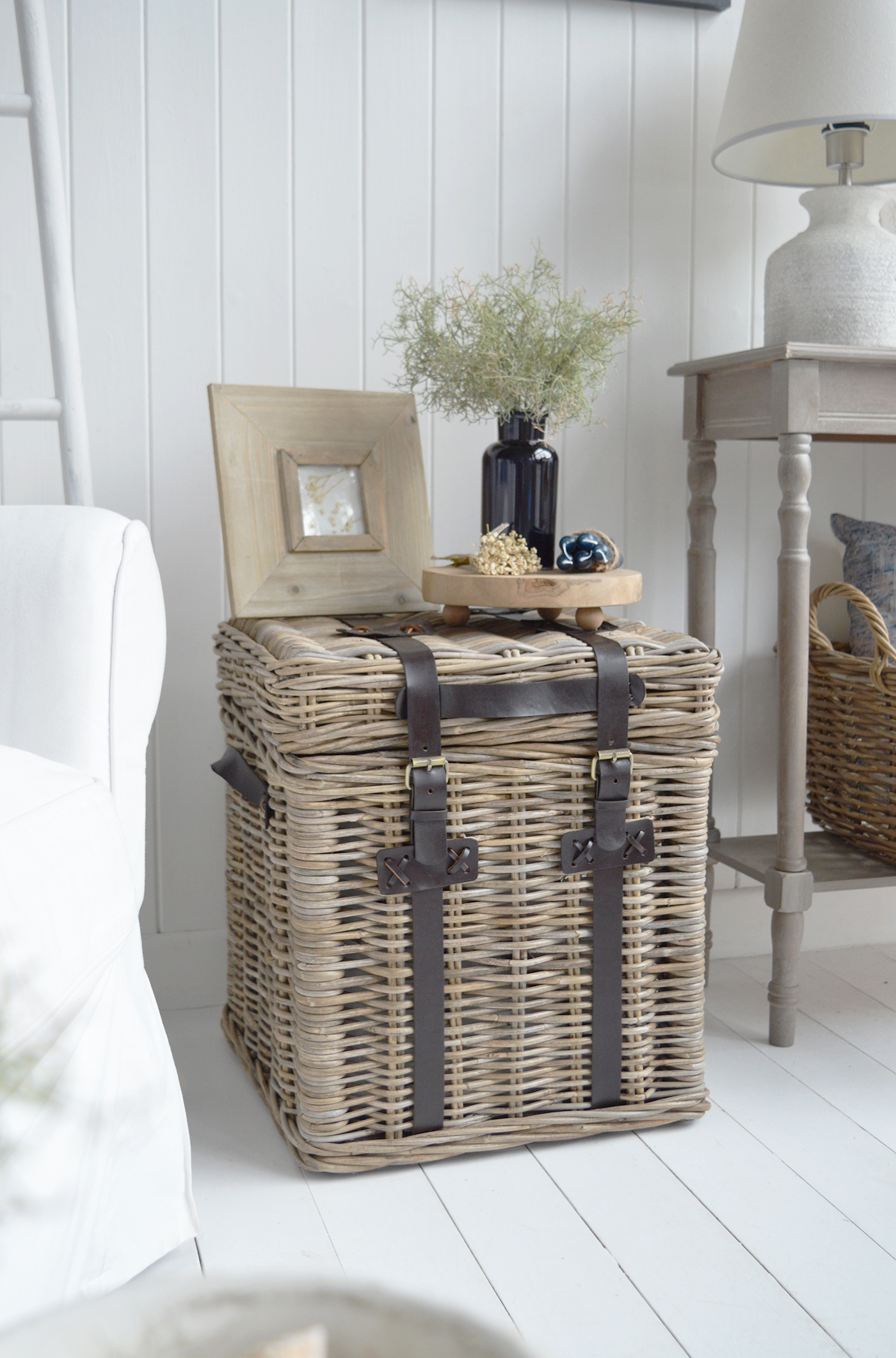 A woven storage trunk doubles as a side table, adding natural texture and useful storage to modern coastal interiors.