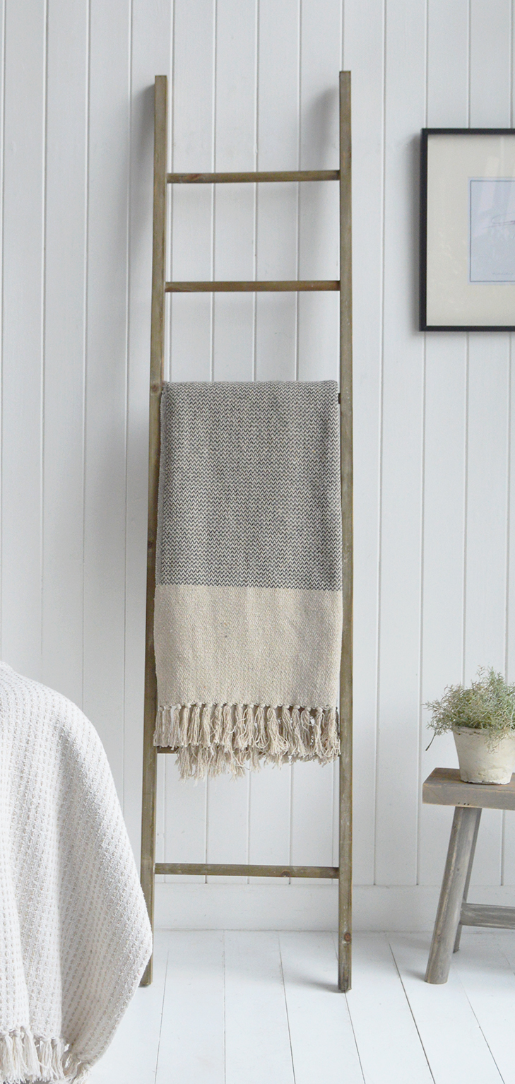 Soft whites and muted neutrals set a calming coastal tone, while rustic wood accents bring in a farmhouse edge. The layered textures of knitted, woven, and fringed fabrics add warmth, creating a serene retreat that feels both elegant and lived-in.