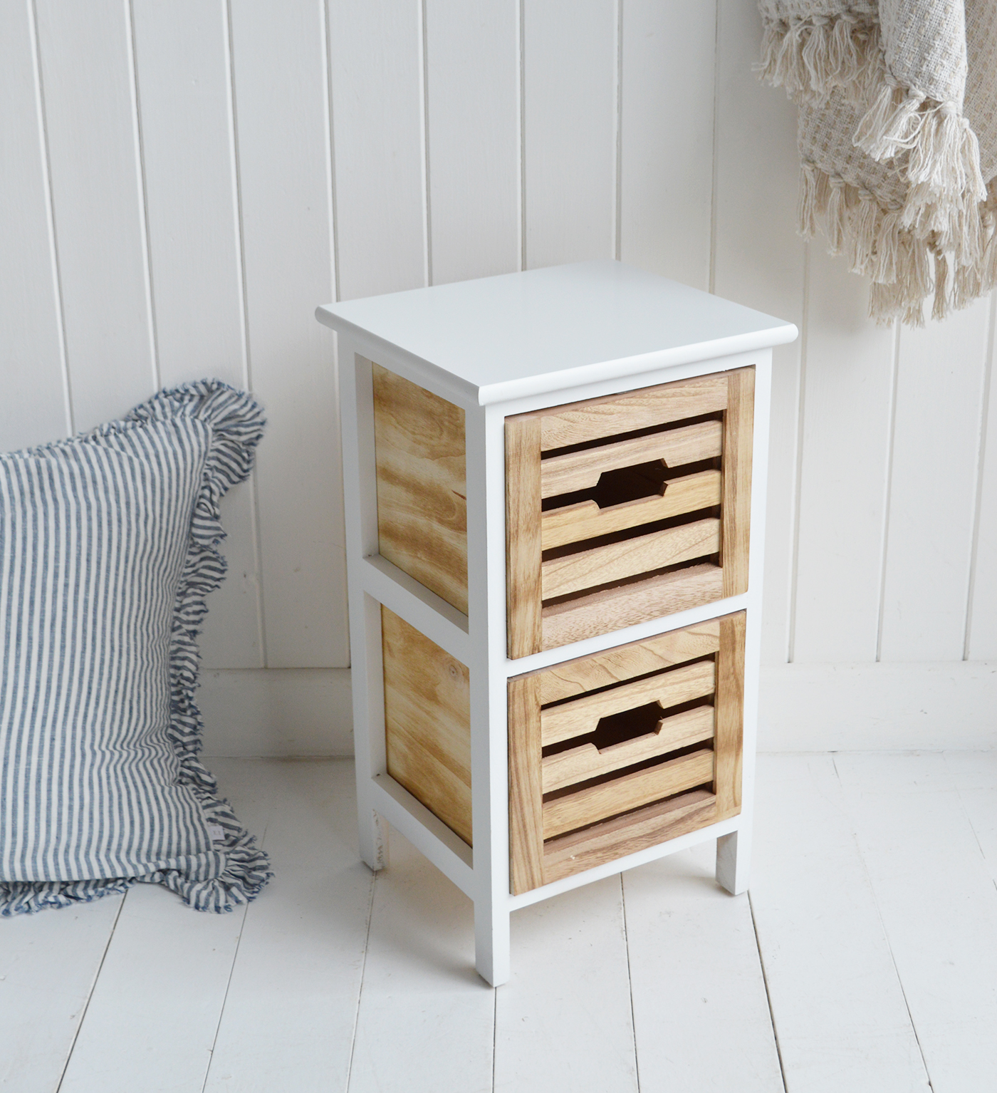 Compact narrow bedside table with white frame and wooden drawers styled in bright coastal New England bedroom