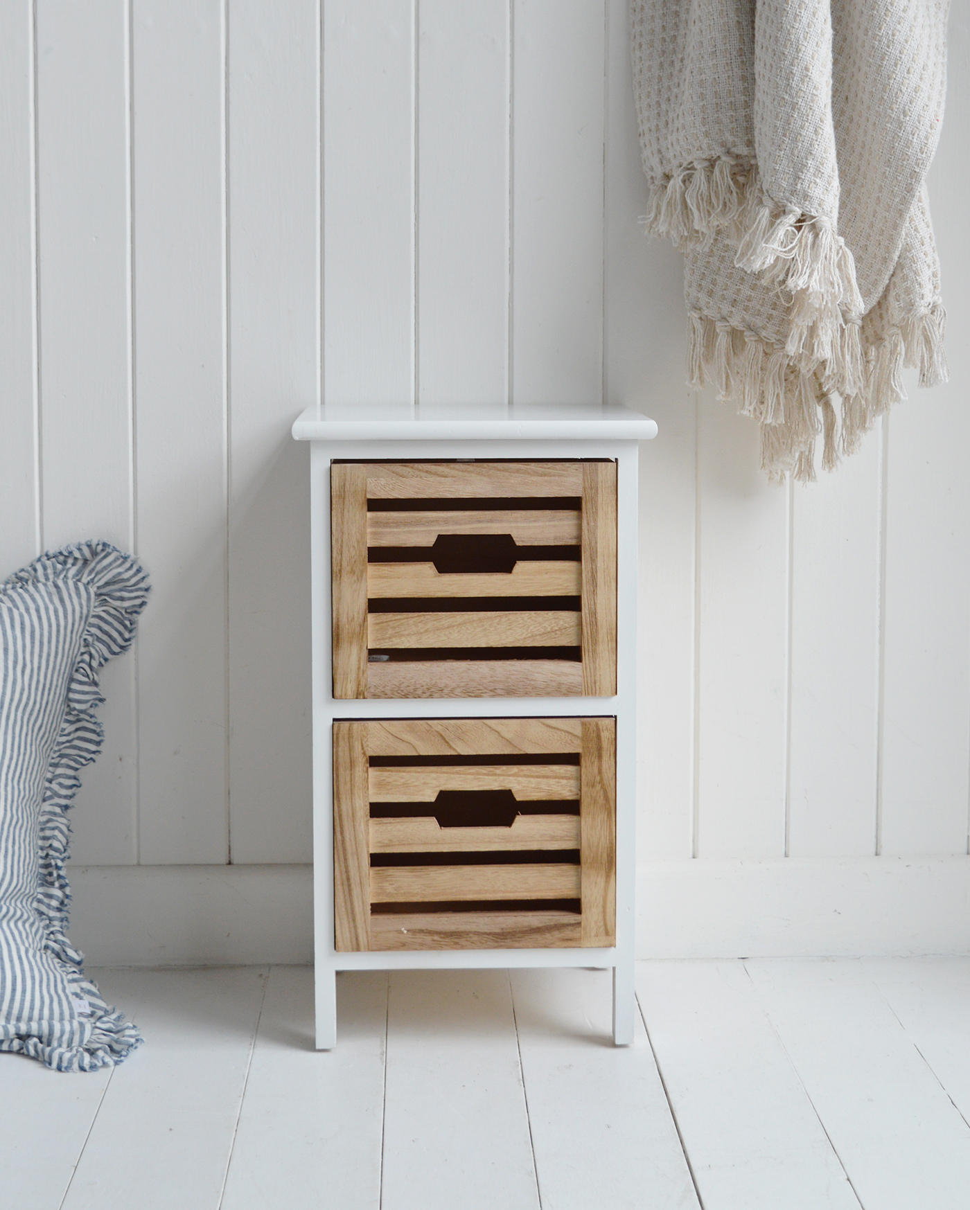 Slim bedside table with crisp white finish and rustic wooden drawers styled with decorative vase and framed print