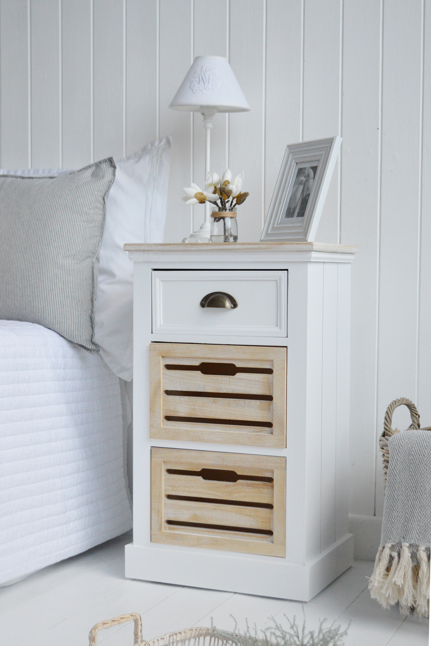 The Southport white bedside table with three drawers in a traditional clapboard finish for a modern coastal feel bedroom interior