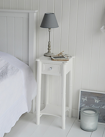 A narrow tall white bedside table with drawer and silver handle. New England White Bedroom Furniture
