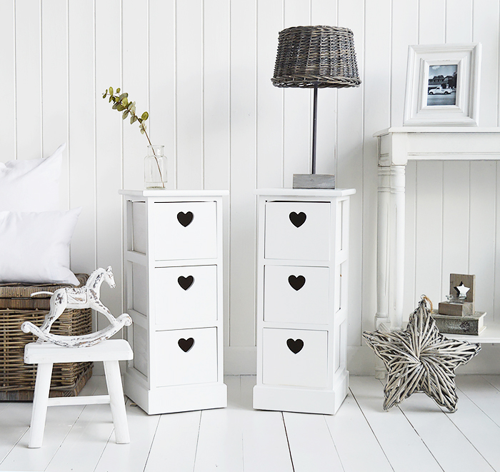 A pair of narrow white bedside tables with three drawers and cut out hearts 25cm wide